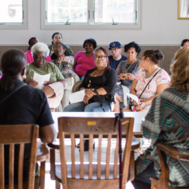 People of various ethnicities and skin tones seated at a meeting in a large, sunny room.