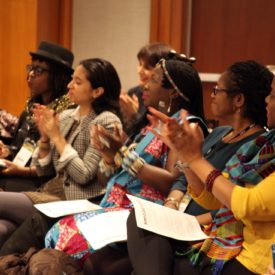 Eight women of color are shown clapping at WOCA's 2016 APAP meeting