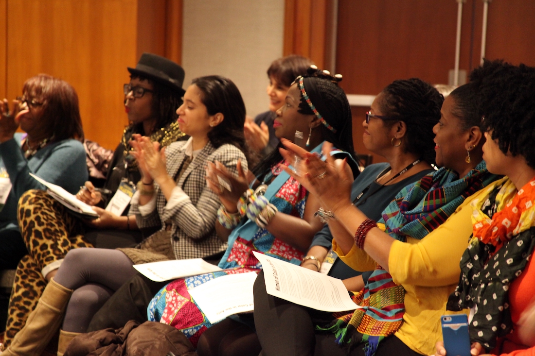 Eight women of color are shown clapping at WOCA's 2016 APAP meeting