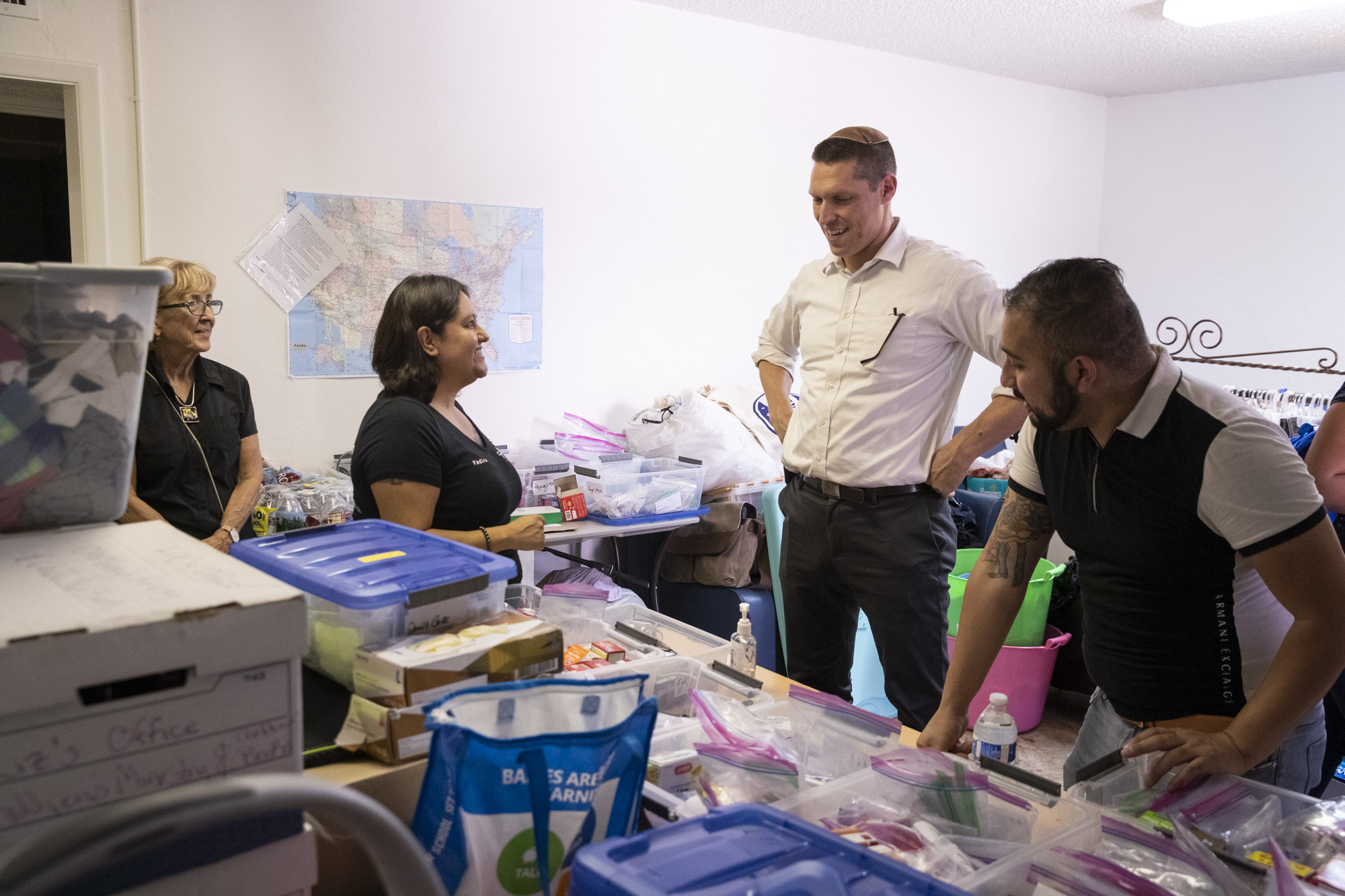 Uri L'Tzedek director Rabbi Yanklowitz shown standing with 3 other staff members in an office crowded with bags of supplies.