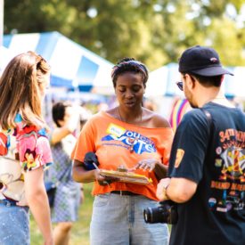 Photo shows woman wearing You Can Vote t shirt, holding a clipboard and talking to a man and a woman.