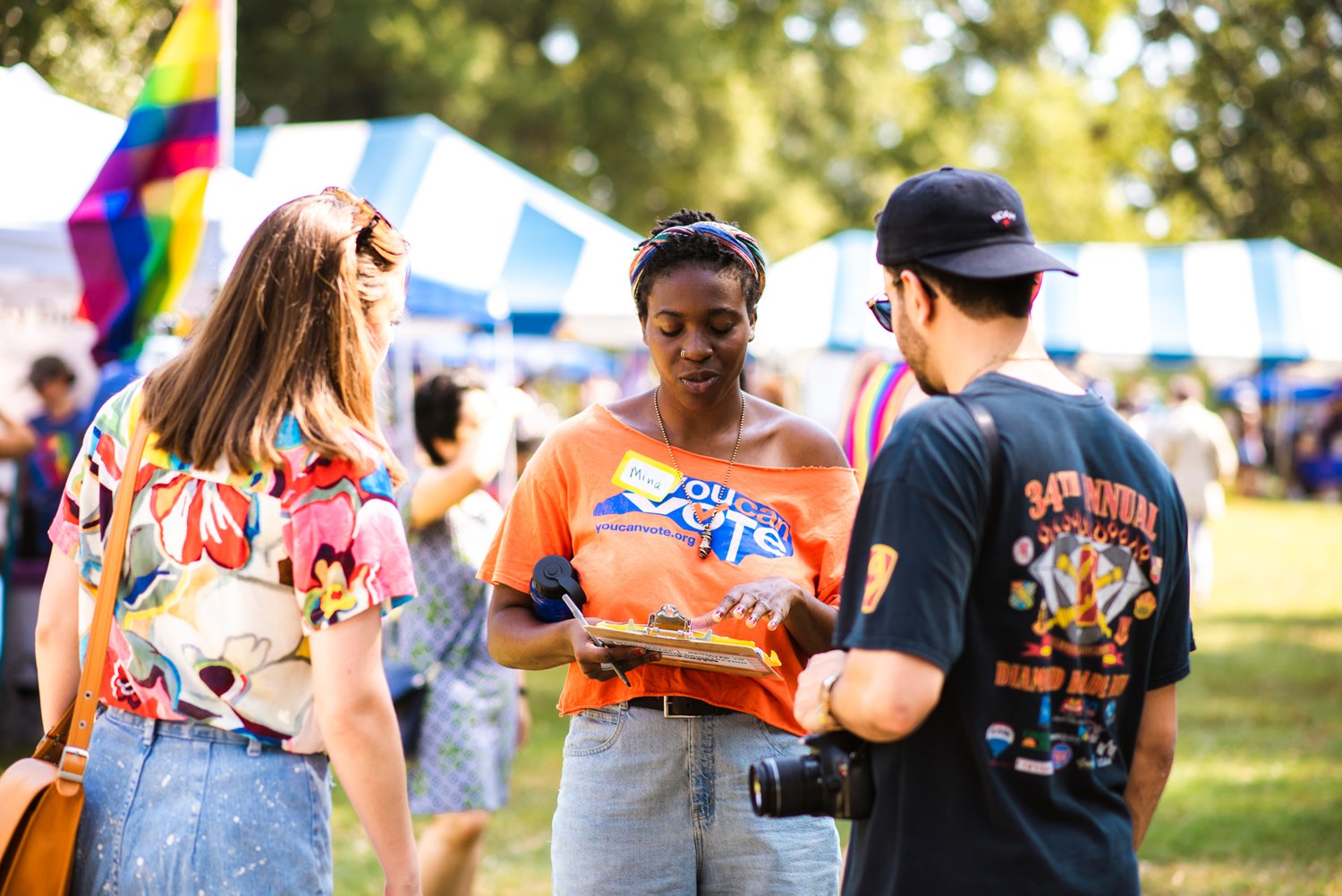 Photo shows woman wearing You Can Vote t shirt, holding a clipboard and talking to a man and a woman.