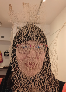 Photo of a woman wearing a close fitting hat and glasses, seen behind the lacy structure of a dried nopal plant